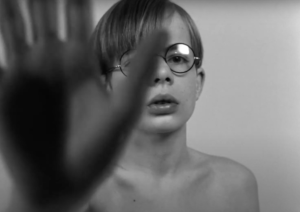  ChatGPT A black and white image of a young boy with glasses, looking towards the camera, with a blurred hand in the foreground partially obscuring his face.