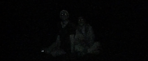 An extremely dark image with the faint outlines of two figures barely visible against the black background.