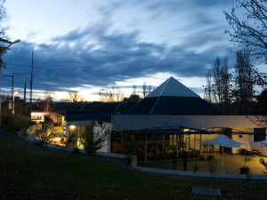 An evening view of a modern art gallery building with an illuminated interior and a darkening blue sky.