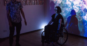 National Young Writers Festival, 2018. Robin is silhouetted against the nebula, mid-spin, with a flare of light just behind their wheelchair frame.